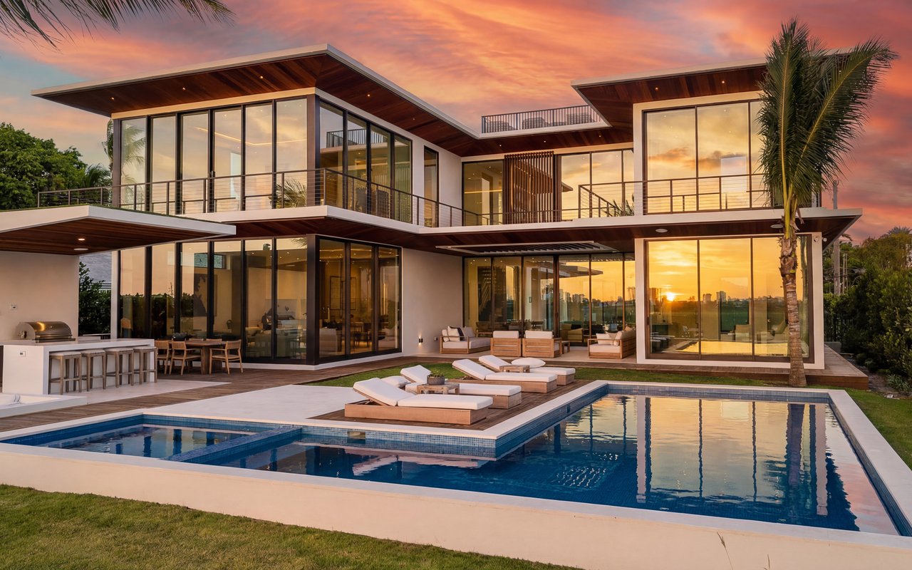Modern two-story waterfront residence at sunset, Miami — floor-to-ceiling impact glass, pool, tropical landscape